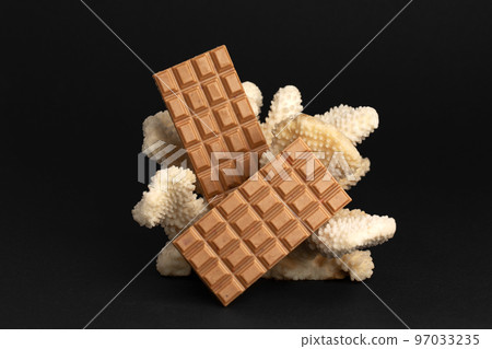 Two large chocolate bars on a coral on black background. 97033235