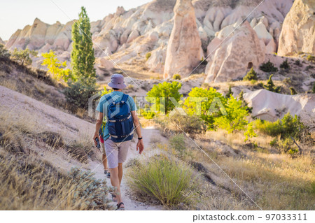 Young man exploring valley with rock formations and fairy caves near Goreme in Cappadocia Turkey Young man exploring valley with rock formations and fairy caves near Goreme in Cappadocia Turkey 97033311