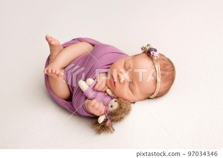 Sleeping newborn girl in the first days of life on a white background. A newborn baby in a purple lilac winding and a headband. Hand, palms of father and mother, parents hold the child. Sleeping newborn girl in the first days of life on a white background. A newborn baby in a purple lilac winding and a headband. Hand, palms of father and mother, parents hold the child. 97034346