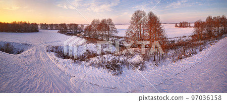 Winter panorama. Snow covered fields, meadows. River, frozen trees, village in evening light. Rural sunset landscape. Dirt road in ice Winter panorama. Snow covered fields, meadows. River, frozen trees, village in evening light. Rural sunset landscape. Dirt road in ice 97036158