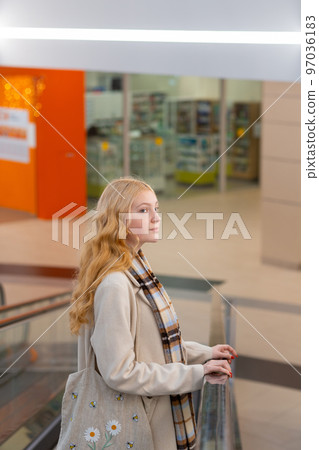 Young woman with long blond hair moving up on escalator 97036183