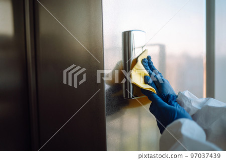 Cleaning and disinfection of the elevator to prevent COVID-19. Worker wearing protective suit sprays. Cleaning and disinfection of the elevator to prevent COVID-19. Worker wearing protective suit sprays. 97037439