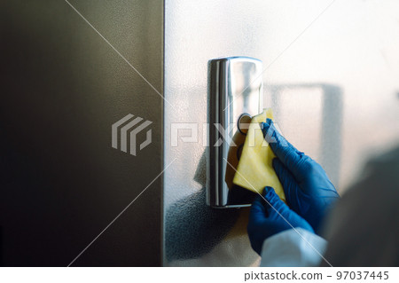 Cleaning and disinfection of the elevator to prevent COVID-19. Worker wearing protective suit sprays. Cleaning and disinfection of the elevator to prevent COVID-19. Worker wearing protective suit sprays. 97037445
