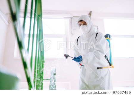 Man in Hazmat suit, protective gloves and goggles use sprayer equipment disinfect the entrance. Man in Hazmat suit, protective gloves and goggles use sprayer equipment disinfect the entrance. 97037459