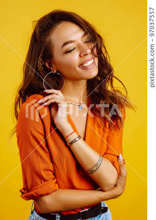 Portrait of young girl posing on yellow background. Pretty woman wears a carrot blouse and jeans. 97037557