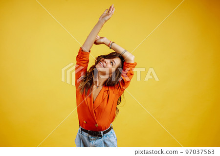 Portrait of young girl posing on yellow background. Pretty woman wears a carrot blouse and jeans. Portrait of young girl posing on yellow background. Pretty woman wears a carrot blouse and jeans. 97037563