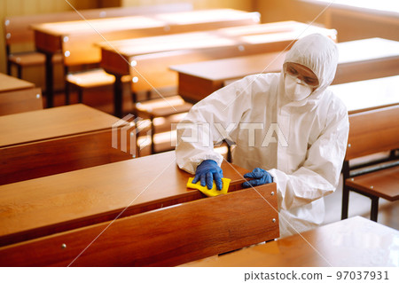 Man in protective hazmat suit washes school desk during coronavirus pandemic. COVID-19. 97037931