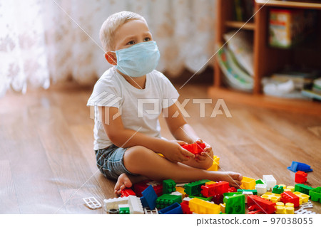 Concept of Covid-19 in quarantine city. Little child in medical mask. plays constructor. 97038055