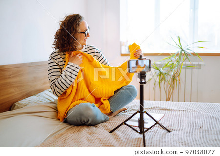 Fashion blogger. Young woman blogger talking with followers, live streaming and showing yellow sweater. Fashion blogger. Young woman blogger talking with followers, live streaming and showing yellow sweater. 97038077