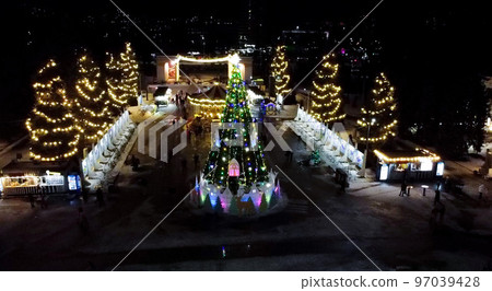 Christmas tree decorated decorative luminous garlands and children's spinning carousel in park in city on winter night. People walking in park. New Year Christmas Christmas tree decorated decorative luminous garlands and children's spinning carousel in park in city on winter night. People walking in park. New Year Christmas 97039428