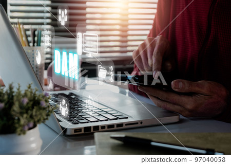 DAM, Digital Asset Management Organization Concept, Person hand using smart phone on office desk with DAM icon  on virtual screen. 97040058