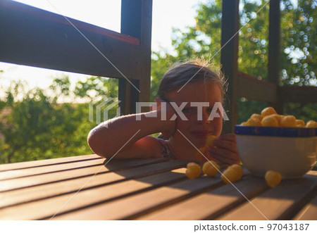 Little girl is sitting on porch in summer. Cheese balls in bowl. Cheese flavoured snacks on a table. Dreamy and romantic image. Summer and happy childhood concept 97043187