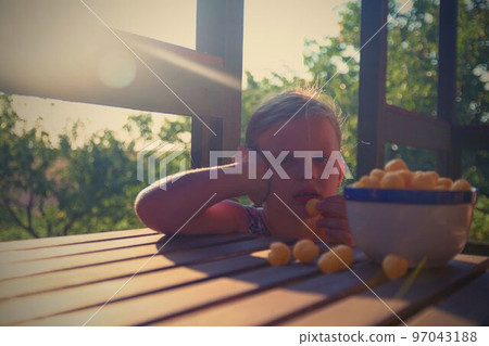 Little girl is sitting on porch in summer. Cheese balls in bowl. Cheese flavoured snacks on a table. Dreamy and romantic image. Summer and happy childhood concept Little girl is sitting on porch in summer. Cheese balls in bowl. Cheese flavoured snacks on a table. Dreamy and romantic image. Summer and happy childhood concept 97043188