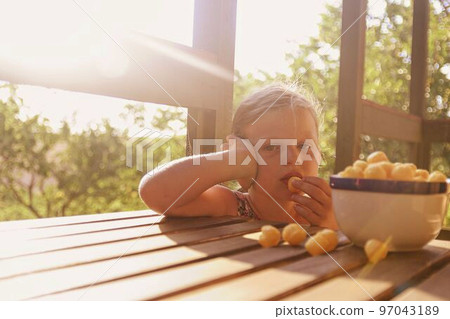 Little girl is sitting on porch in summer. Cheese balls in bowl. Cheese flavoured snacks on a table. Dreamy and romantic image. Summer and happy childhood concept Little girl is sitting on porch in summer. Cheese balls in bowl. Cheese flavoured snacks on a table. Dreamy and romantic image. Summer and happy childhood concept 97043189
