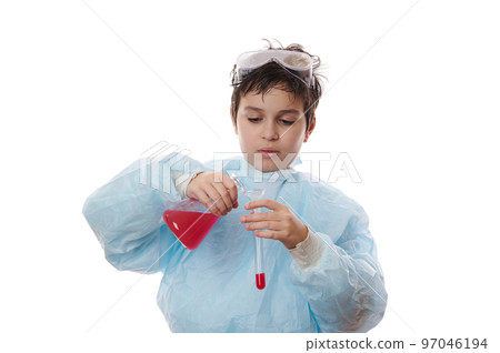 Focused teenage boy, school child, young scientist-chemist in lab coat, pours red liquid chemical substance through glass funnel into test tube on white background. Learning chemistry. Back to school 97046194
