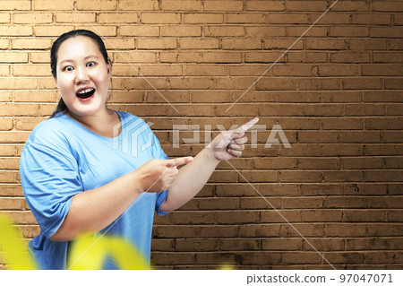 Asian fat overweight woman with an excited expression pointing to something 97047071