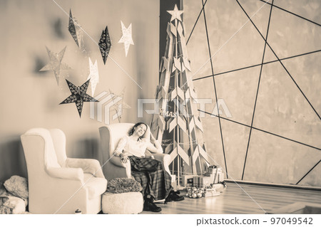 beautiful young woman sitting in a chair near a stylized Christmas tree. black and white photo beautiful young woman sitting in a chair near a stylized Christmas tree. black and white photo 97049542