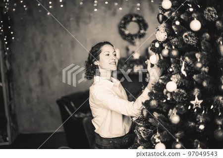 beautiful young woman decorating Christmas tree in her living room. black and white photo beautiful young woman decorating Christmas tree in her living room. black and white photo 97049543