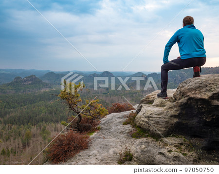 Man sitt on cliff edge and looking to rising sun above valley Man sitt on cliff edge and looking to rising sun above valley 97050750