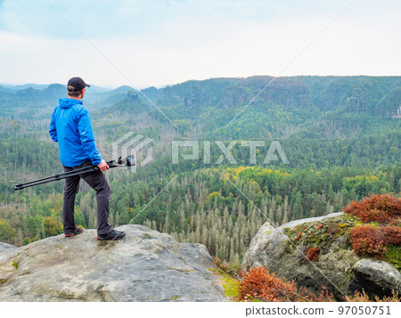 Photographer with folded tripod on end of cliff thinking. NAtural forestry landscape Photographer with folded tripod on end of cliff thinking. NAtural forestry landscape 97050751