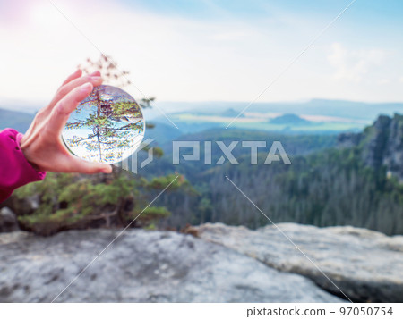 Hand holding glass sphere in front of valley. Looking through glass lens 97050754