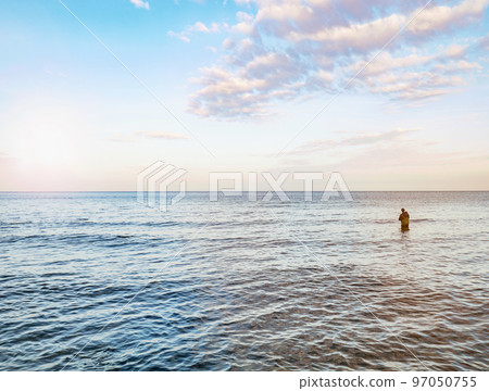 Fisher man stay in the water and pulling bait on his fishing rod. Baltic shore Fisher man stay in the water and pulling bait on his fishing rod. Baltic shore 97050755