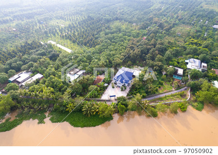aerial view of Villa house in the middle of the garden with blue tile roof and the river at Mekong river delta VietNam countryside, Thai house building style. aerial view of Villa house in the middle of the garden with blue tile roof and the river at Mekong river delta VietNam countryside, Thai house building style. 97050902