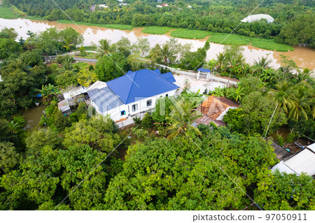 aerial view of Villa house in the middle of the garden with blue tile roof and the river at Mekong river delta VietNam countryside, Thai house building style. aerial view of Villa house in the middle of the garden with blue tile roof and the river at Mekong river delta VietNam countryside, Thai house building style. 97050911