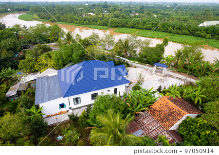 aerial view of Villa house in the middle of the garden with blue tile roof and the river at Mekong river delta VietNam countryside, Thai house building style. aerial view of Villa house in the middle of the garden with blue tile roof and the river at Mekong river delta VietNam countryside, Thai house building style. 97050914