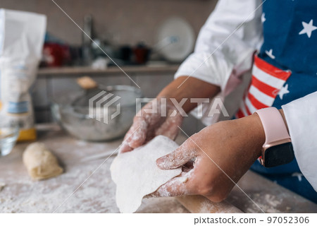 Young housewife in an apron kneads dough with her hands. 97052306
