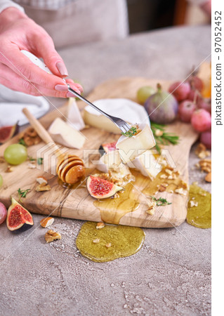Woman puts on a fork piece of Camembert or brie cheese at domestic kitchen 97052452