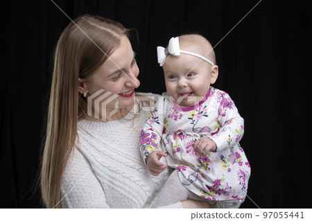 Mom holds a little happy daughter in her arms. Motherhood. 97055441