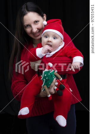 Mom and little child at Christmas. A woman holds her son in her arms, who is dressed in Santa Claus clothes. 97055451