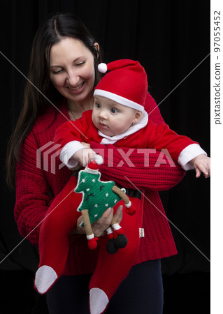 Mom and little child at Christmas. A woman holds her son in her arms, who is dressed in Santa Claus clothes. Mom and little child at Christmas. A woman holds her son in her arms, who is dressed in Santa Claus clothes. 97055452