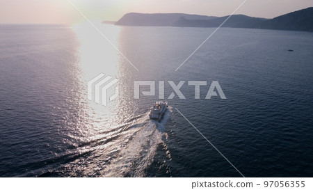 White luxury yacht sails on the ocean. Shooting from a drone as a small light sea vessel, leaving a trail of foam and waves along the sea dark water surface White luxury yacht sails on the ocean. Shooting from a drone as a small light sea vessel, leaving a trail of foam and waves along the sea dark water surface 97056355