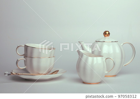 Beautiful white still life with white dishes for tea, coffee, with a golden spoon on a white background Beautiful white still life with white dishes for tea, coffee, with a golden spoon on a white background 97058312