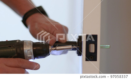 A man's hand attaches to the door handle with screws and a screwdriver, close-up 97058337