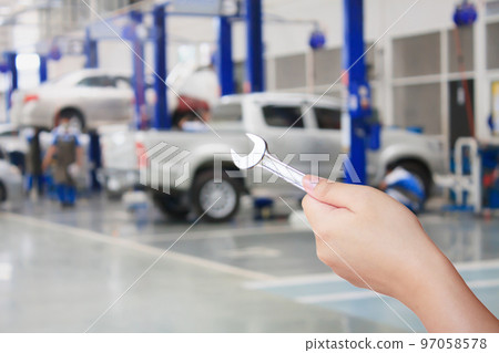 Technician holding a wrench with car repair service center background Technician holding a wrench with car repair service center background 97058578