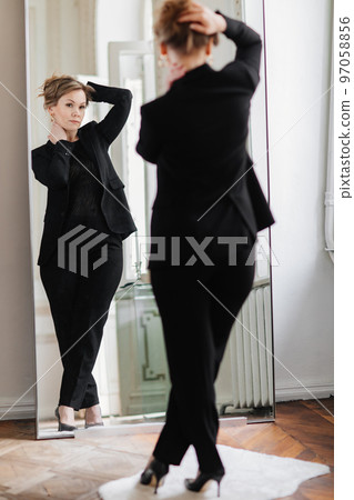 an attractive sexy woman in a black suit looks at her reflection in the mirror 97058856