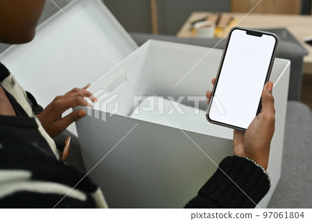 Close up view of female customer unpacking parcel f and using smart phone for giving feedback to shop 97061804