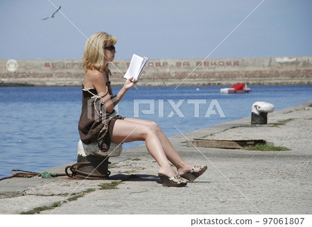 On the pier girl reading a book and sunbathing. 97061807