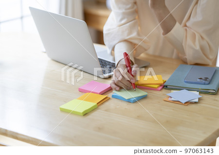 Young woman's hand making a note on a sticky note 97063143