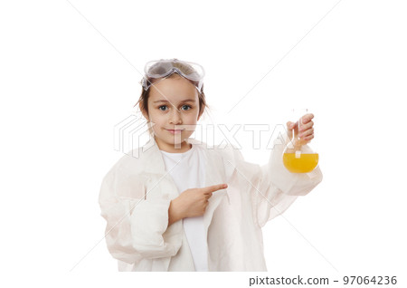 Smart elementary school child, lovely little girl in lab coat, points at laboratory flask with yellow chemical solution, shows the ongoing chemical reaction, looking at camera, on a white background Smart elementary school child, lovely little girl in lab coat, points at laboratory flask with yellow chemical solution, shows the ongoing chemical reaction, looking at camera, on a white background 97064236