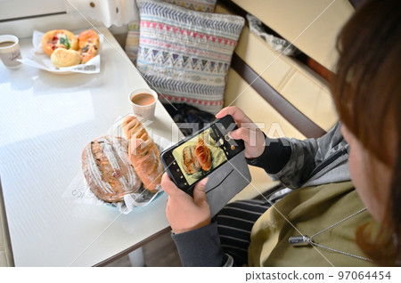A woman stylishly photographing a meal in a camper van with her smartphone Deli bread A woman stylishly photographing a meal in a camper van with her smartphone Deli bread 97064454
