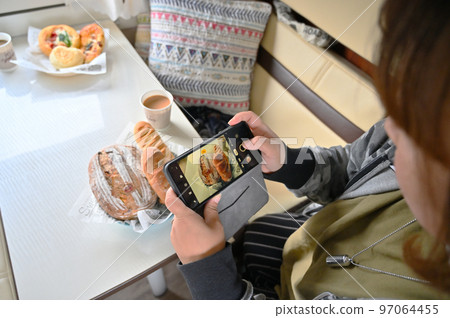 一位女士用她的智能手機 Deli 麵包在露營車裡時尚地拍攝一頓飯 一位女士用她的智能手機 Deli 麵包在露營車裡時尚地拍攝一頓飯 97064455