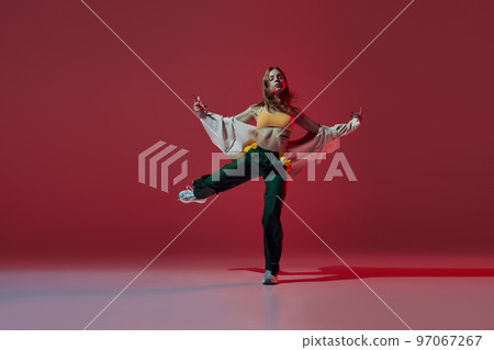 Dynamic portrait of young girl dancing hip-hop or contemporary dance isolated on dark red background. Experimental dance. Music, dance, active lifestyle, fashion, style Dynamic portrait of young girl dancing hip-hop or contemporary dance isolated on dark red background. Experimental dance. Music, dance, active lifestyle, fashion, style 97067267