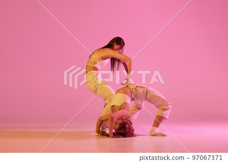 Modern dance art. Young girls, couple of dancers in sports style clothes dancing experimental dances isolated over light pink background in neon. Concept of music, emotions, dance Modern dance art. Young girls, couple of dancers in sports style clothes dancing experimental dances isolated over light pink background in neon. Concept of music, emotions, dance 97067371