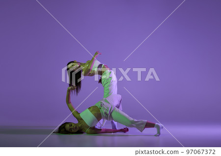 Studio footage of dancing young girls. Stylish performance. Two young women in expressive contemporary dance isolated over purple background. Studio footage of dancing young girls. Stylish performance. Two young women in expressive contemporary dance isolated over purple background. 97067372