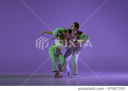 Dance performance. Stylish female dancers at contemporary choreography dance class isolated over crystal purple background. Style, youth, music and fashion 97067395