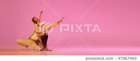 Two stylish female dancers in casual style clothes dancing contemporary choreography dance over crystal pink background. Concept of modern art, creativity, fusion Two stylish female dancers in casual style clothes dancing contemporary choreography dance over crystal pink background. Concept of modern art, creativity, fusion 97067400